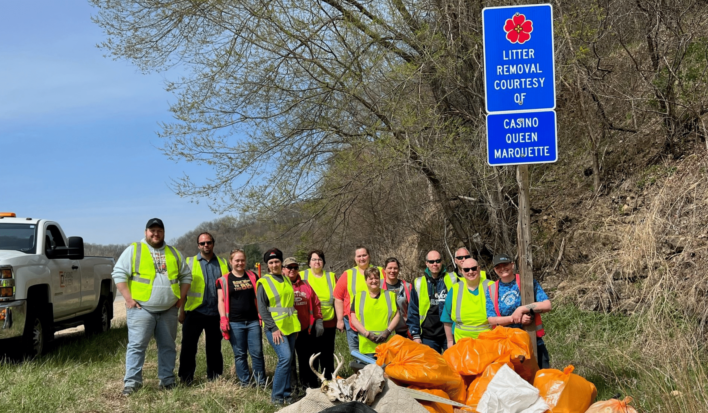 Group shot of Casino Queen Marquette team members standing with their picked up litter. Sign reads "Litter removal courtesy of Casino Queen Marquette"